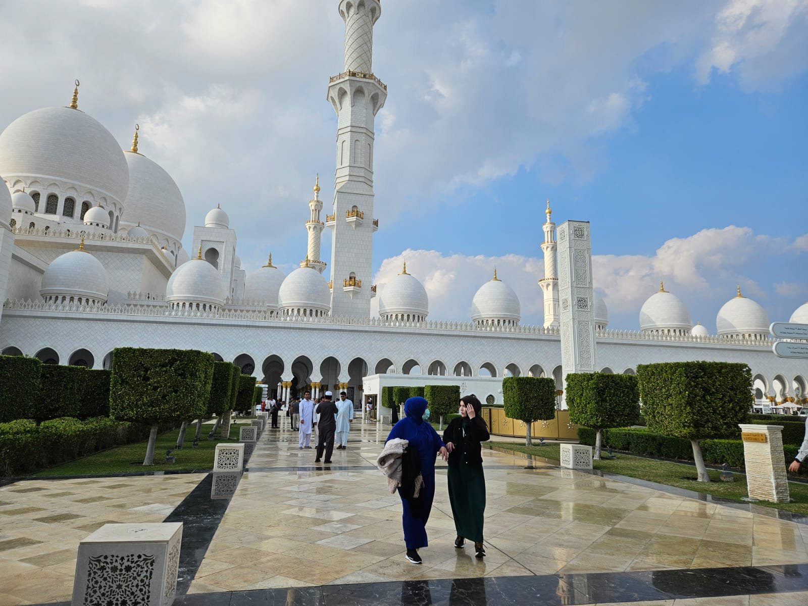 People walking in front of the Sheikh Zayed Grand Mosque on a clear day.